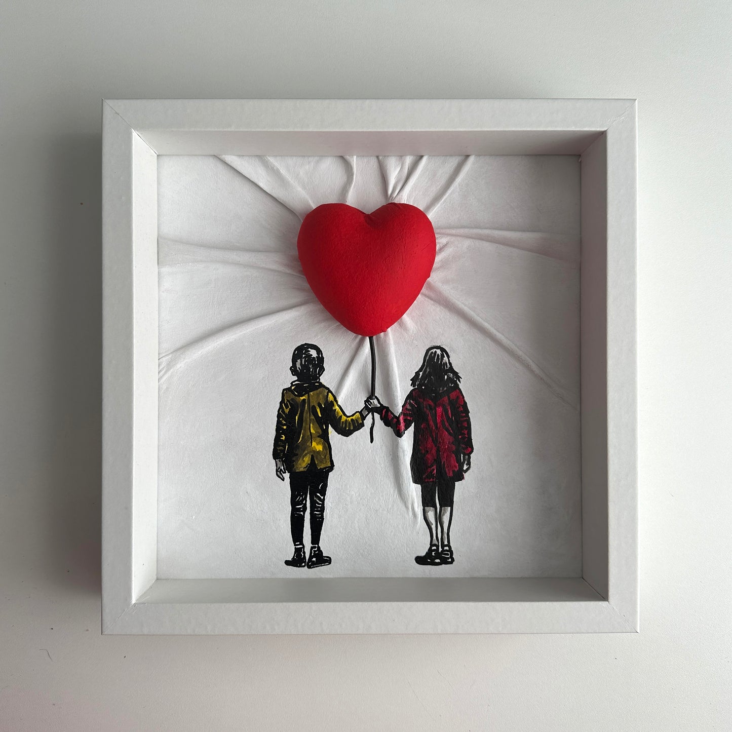 Fashionable and modern Novasuede leather sculpture of a girl and boy with a red heart balloon, framed and ready to hang.