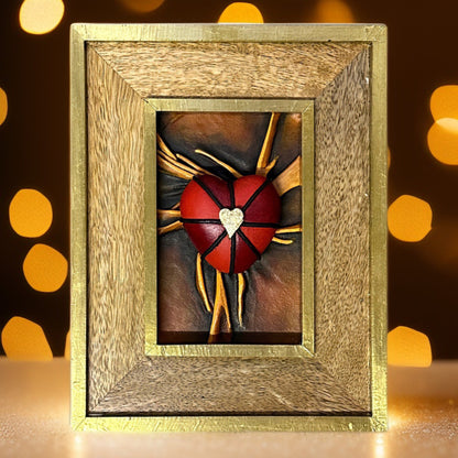 Handcrafted leather heart sculpture with striking black, red, and gold details, framed in a luxurious gold leaf-finished frame.