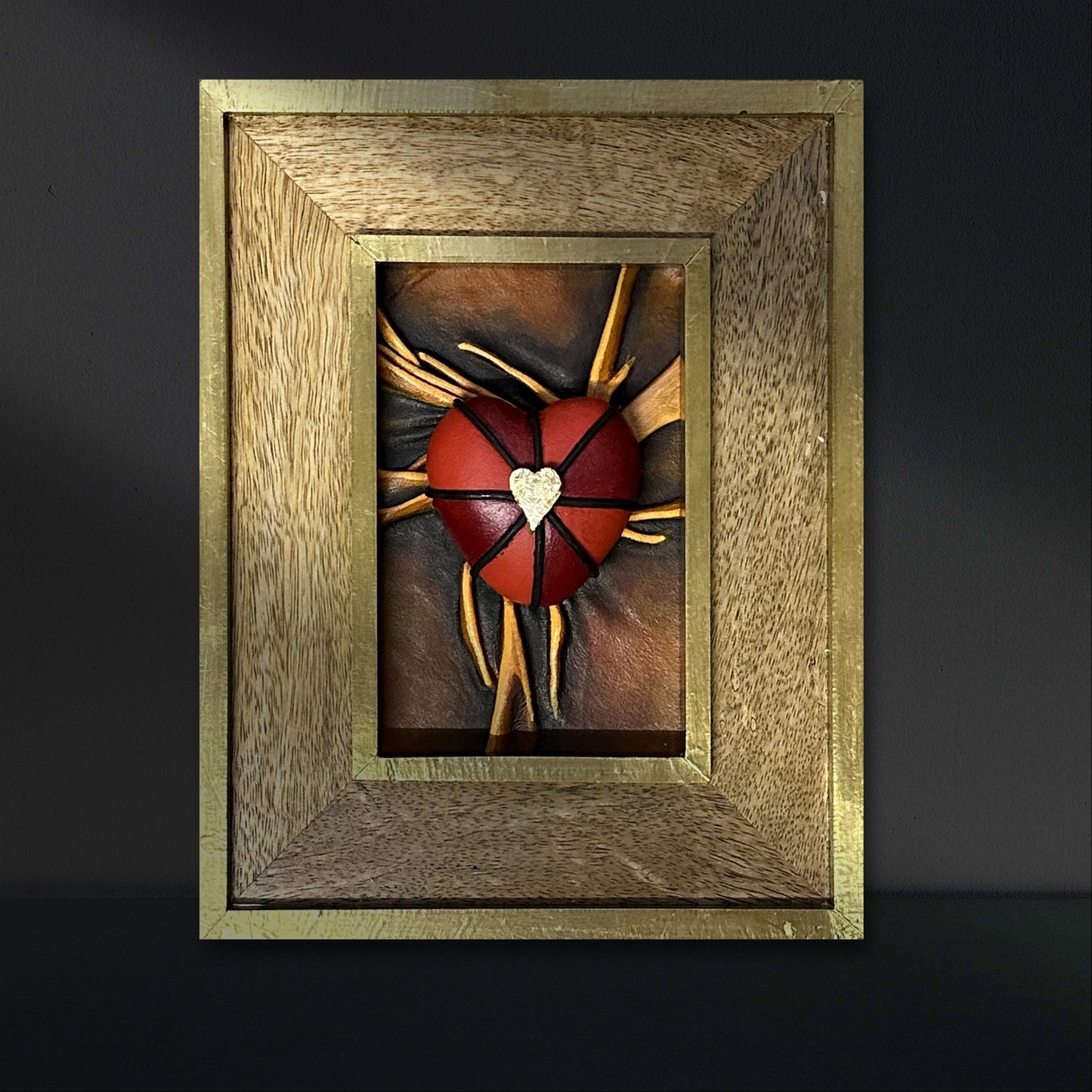 Exquisite leather heart artwork, meticulously painted with black, red, and gold, housed in an elegant wooden frame.